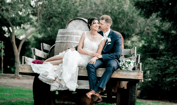 A bride and groom sitting on a wagon in front of a vineyard.