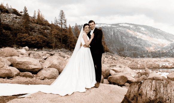 A bride and groom standing on rocks in front of a lake.