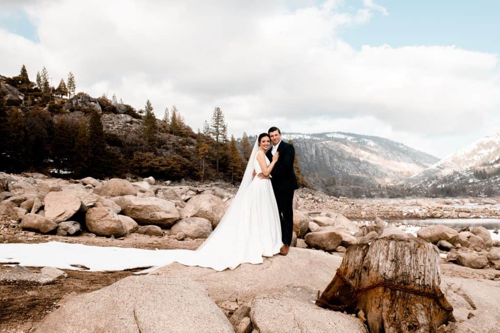 A bride and groom posing on rocks near a lake in yosemite.