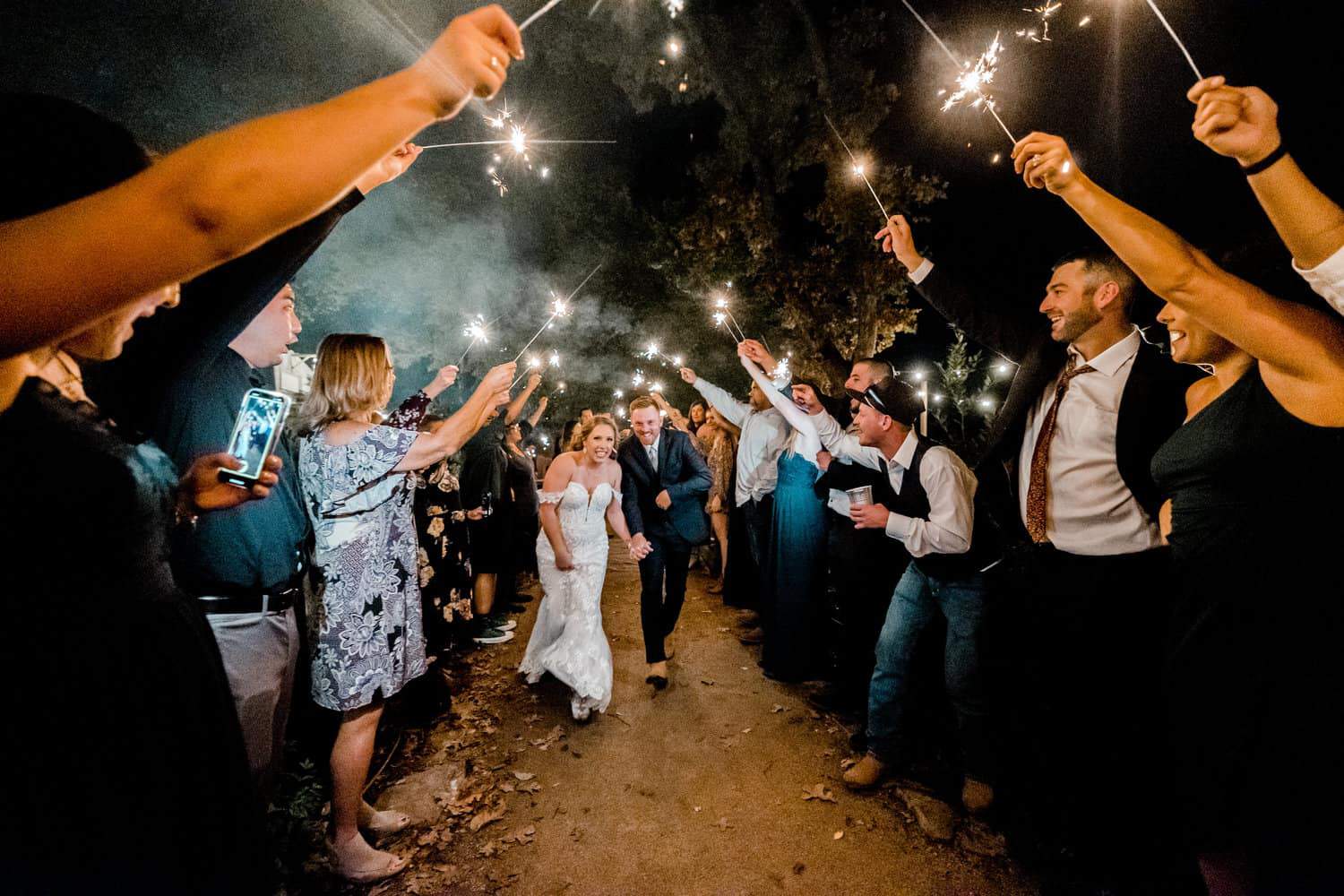 A bride and groom walking down a path with sparklers in their hands.
